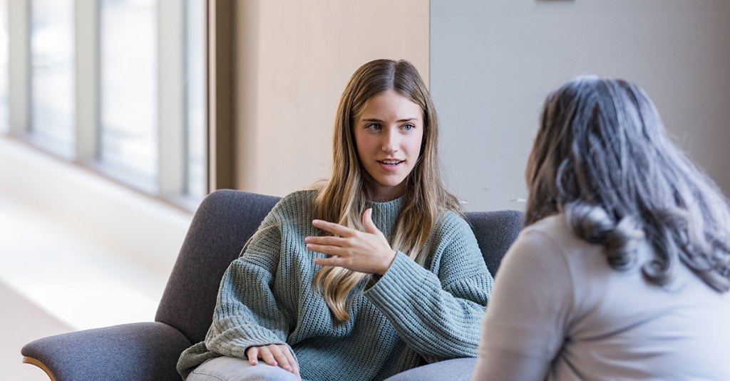 two woman talking while sitting on chairs