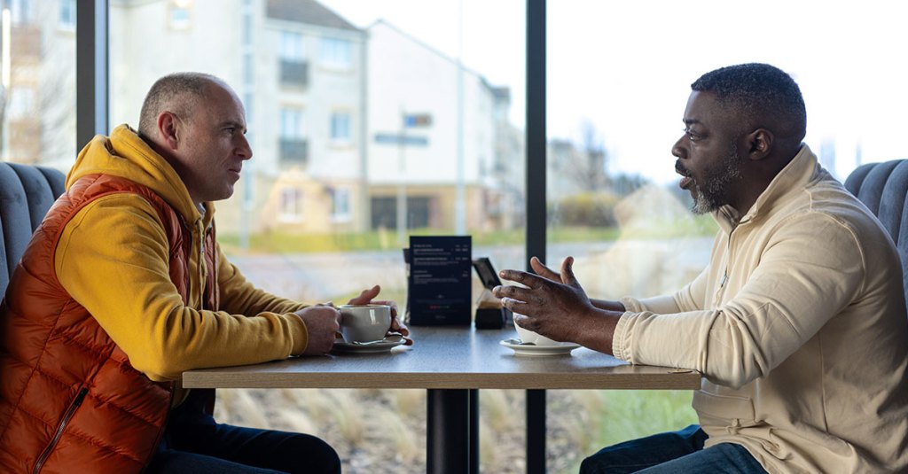 two men sitting across from each other at a table in a restaurant