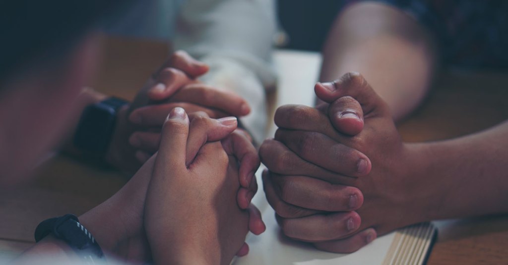 3 hands on table folded in prayer